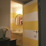 glass pot black tiled flooring laminate wood flooring yellow and white door wall black cabinet white and yellow horizontal striped wall white wall mounted sink round mirror