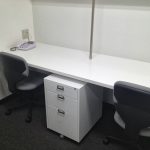 desk for two persons with cabinet and drawers in the center two units of movable office chairs two telephone sets