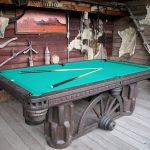 western metal-base pool table with blue surface and two billiard sticks wood planks wall in rustic style