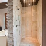 large walk in shower no door with high and large ceiling shower head warm and light cream natural stone tiles for floors and wall system  a pair of wall mounted shower heads a bathtub