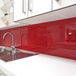 exotic red glossy acrylic backsplash design in modern kitchen idea with white upper cabinetry and white drawesr for main cabinet with double sinks and curved faucet