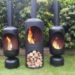 triple black chiminea fire pit idea in tube style with no legs with chimney on grassy meadow with greenery