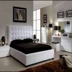 Quuen sized bed furniture with higher white leather headboard dark brown bedding and dark brown pillows a pair of white minimalist bedside tables a white bedroom vanity with white framed mirror