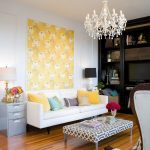 comfortable interior design with white sofa and colorful cushions and chandelier and wooden flooringa nd wing chair and yellow wallpaper