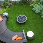 elegant backyard patio design idea with grassy meadow and gray half round bench and fire pit and white bench and wooden deck