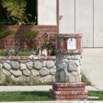 sweet combination of stone and red brick mailbox idea with mini garden on green grassy meadow before a house