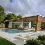 luxurious single storey house design with wooden siding and open plan and sloping facade with swimming pool and concrete patio deck