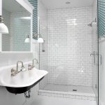 Floating kohler sink with a pair of faucets for a modern bathroom a frameless mirror a pair of vanity lamps frameless glass door shower space with wall mounted showerhead fixture
