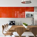 elegant and stylish kitchen design with orange cabinet and white siding paint and wooden dining set with small potted indoor plants and pendants