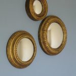 golden framed small convex mirror which are available in different sizes mounted on gray painted wall