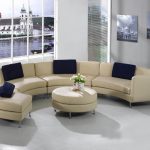 Half circle couch in cream with dark blue throw pillows a round cream cushioned center table with metal legs