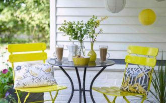 traditional porch idea white siding exterior walls black painted wood board floors bright yellow chairs black wrought iron table with round glass top