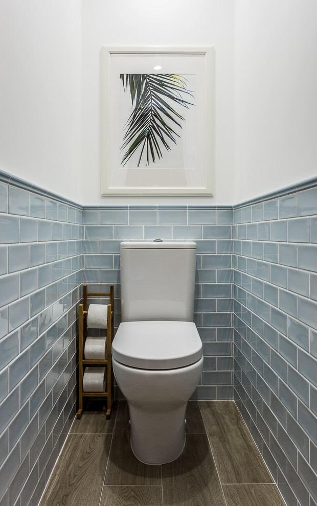 small beach style bathroom light blue tiled walls white painted concrete walls white toilet wood tissue stand wood like tiled floors