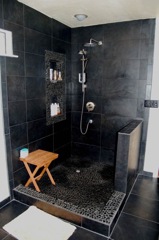 small bathroom in black black tiled walls black stoned floors wood shower bench with x base wall mounted shower fixture recessed shelves
