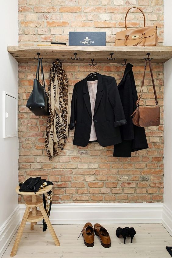 small walk in closet idea red brick accent wall wood shelf with hooks under white walls and floors wood stool