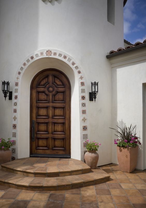 Mexican exterior design curved top wooden front door curved top front gate terra cotta tile floors white finish stucco wall