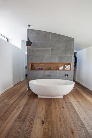 white tub recessed wood shelf concrete wall partition organic wood floors