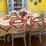 geomatric patterned table cloth white painted wooden chair love shaped pendant red ceramic pot wooden varnished floor yellow painted wall white drinking cups white ceramic soup bowl