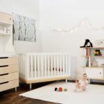 hardwood flooring white rug simple white wooden crib white wall white and light brown wood open shelf white and light brown cabinet railing wall lamp flower picture