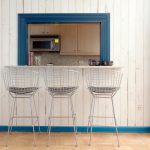 metal stools with grey seat white wood outdoor wall with turquoise trim wood-like tiled flooring dark blue framed kitchen pass through wood upper cabinets grey granite counter