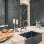 classic kitchen design with white marble countertop with deep black sink and stainless steel faucet two candle  stand fixtures two bottles of wine a wine glass some pieces of bread and a pile of flat plates