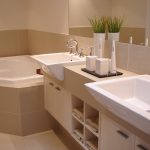 warm and minimalist bathroom design with small white corner tub with light brown tub-wall minimalist bathroom vanity with large double sinks and faucets a frameless mirror for bathroom