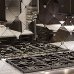 adorable diamong patterned antique mirror backsplash with cook top on white cabinetry with amazing lighting