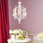 modern luxurious funky chandelier above white round table in pink room design with red curtain and flower vas aside bedding set