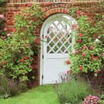 arched white lattice fence design around reddish brick wall with beautiful flower decoration with meadow grass