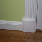 baseboard trim styles in white combined with green painted wall and hardwood flooring