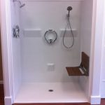 simple and minimalist walk in shower without door in white color wall mounted showerhead a heldhand showerhead two floating shelves a floating wood bench for bathing