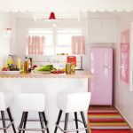 Small kitchen with cute decoration such as pink covered refrigerator pink window curtains a kitchen island with wooden top and white barstools rainbow mat wood floors