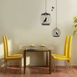 Wall art depicting the birds on the cage a set of dining furniture consisting yellow dining chairs and dining table