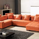 Larger orange leather sectional with single chaise and orange throw pillows a low profile coffee table in black coat grey wool rug a modern white console for displaying some ceramic vase ornaments