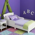 Nantucket-white-toddler--bed-by-kidkraft-from-strong-and-durabe-rubber-wood-with-smooth-white-lines-and-regular-crib-mattress-surrounded-with-purple-color-wall