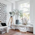 vintage white interior with black white wallpaper with tripod floor lamp and white chair and white console and potted plant and glass window and wooden floor