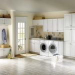 wide and white laundry room idea with white washed flooring and cabinetry and glass door and basket shelves