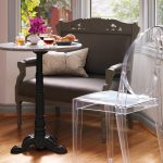 Smaller round white marble top bistro table with classic black wooden base transparent plastic chair an armchair with white throw pillow