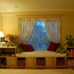 simple white bay window couch design with sheer white curtain and red cushion design with storage and bookshelves and creamy area rug