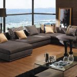 Most comfortable sectional sofa with chaise in one end together with comfortable rug under glass coffee table and standing lamp and wall mounted shelves
