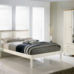 White minimalist bed frame with headboard a white cloth closet storage with mirror door a vertical drawer system in white white bedside table with drawers in white