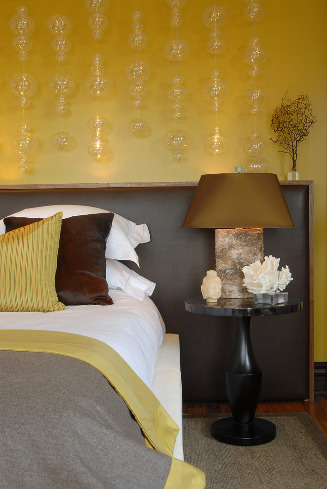 trendy & contemporary bedroom mustard yellow walls with glass bubbles with lighting inside large dark leather headboard white bed linen black finishing bedside table