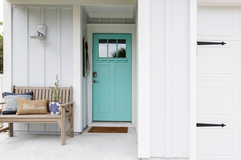 tropical themed front porch idea coastal blue front door with upper black glass soft wood bench with back multicolored accent pillows pale blue exterior walls white floors