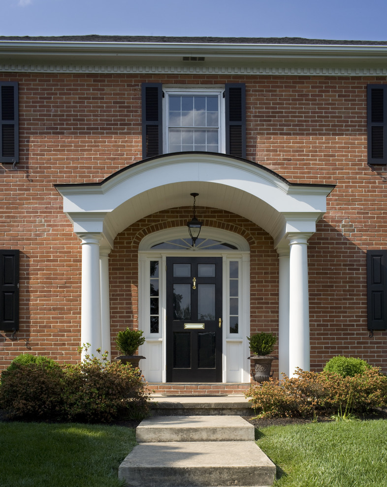 traditional entryway with traditional black front door accented by sidelights and curved top huge white entry gate red bricks exterior walls