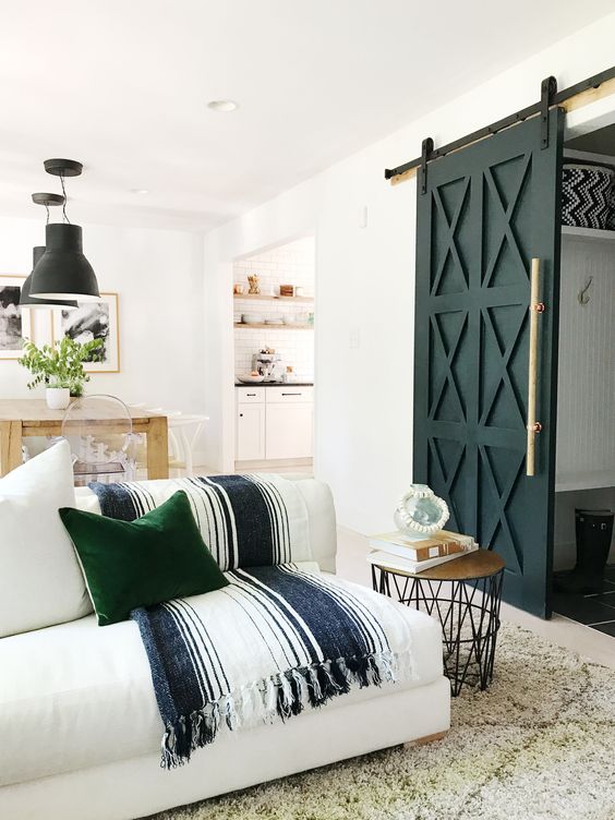 rustic farmhouse living room idea modern barn door with modern door pull white couch with striped blanket green throw pillow wooly white rug wood top side table with thin metal stick legs