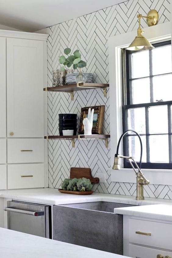 white herringbone tile backsplash with black grout farmhouse sink brass lamp over the sink white cabinetry wooden display racks