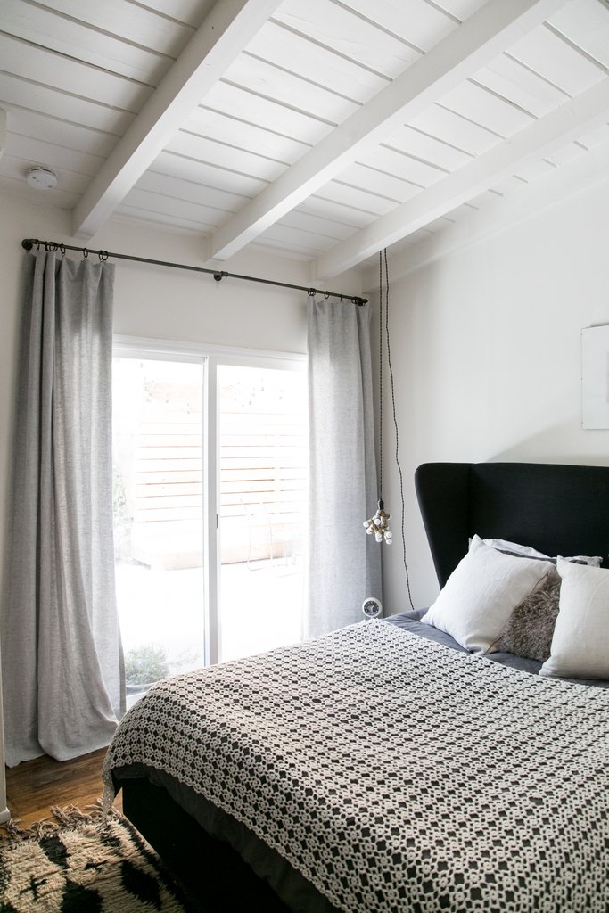 exposed wood beams in white wood plank ceilings in white bed frame with black headboard monochrome bed linen ultra light gray curtains