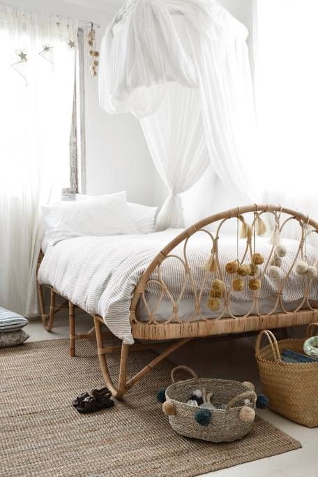 rattan bed frame with foot board woven rug two woven baskets white draperies white bed drapery