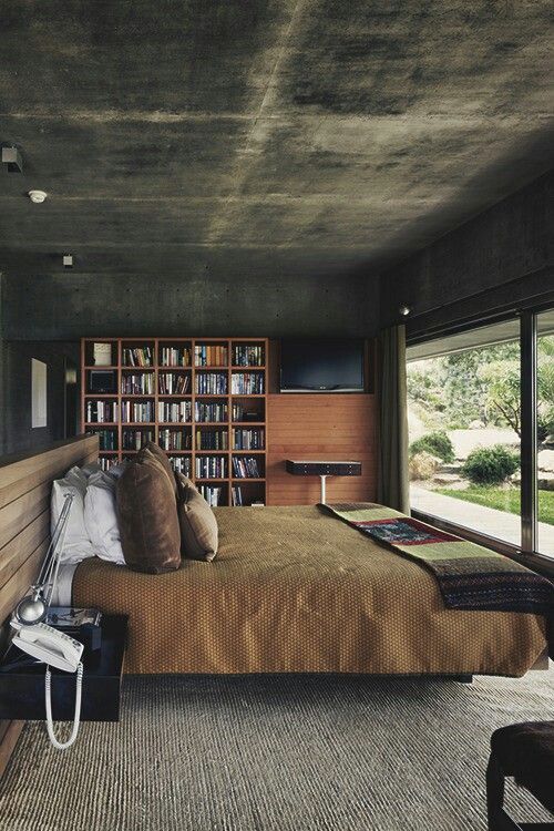 modern bedroom design with bare concrete ceilings and walls wood bookshelves modern bed with wood paneling headboard brown bedding linen huge glass window