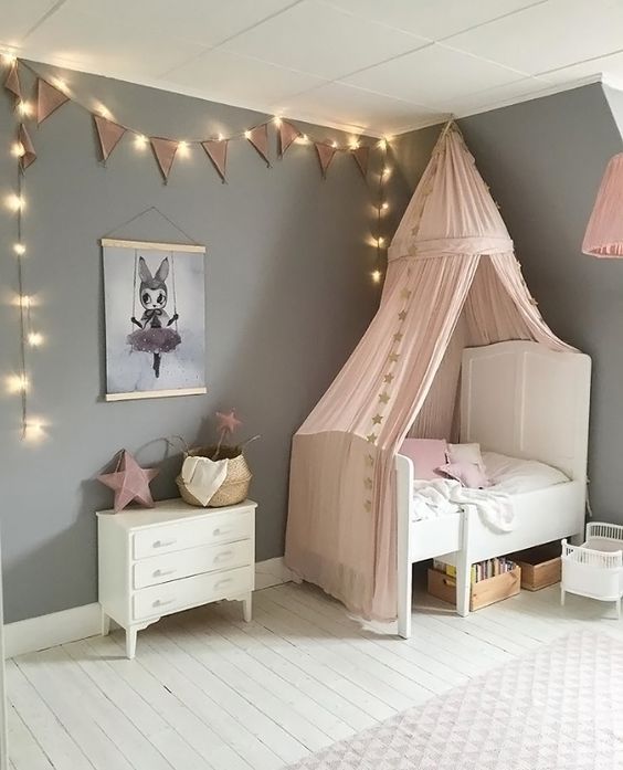little girl's room white bed frame with headboard white dresser gray walls with string lamp ornament white wood plank floors blush pink bed drapery
